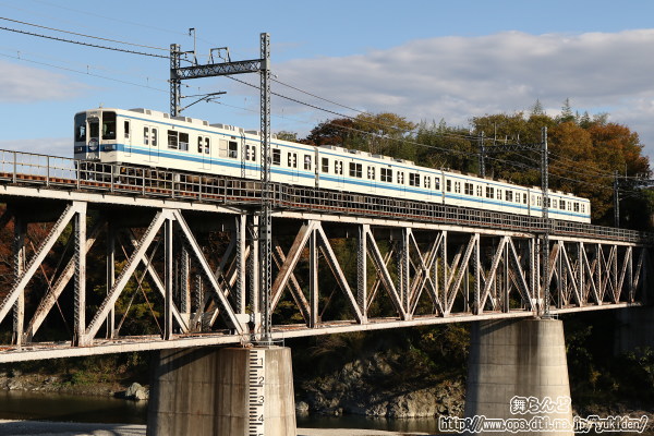 紅葉シーズンを迎えた荒川橋梁を渡る新駅開業記念のヘッドマークを付けた8198F