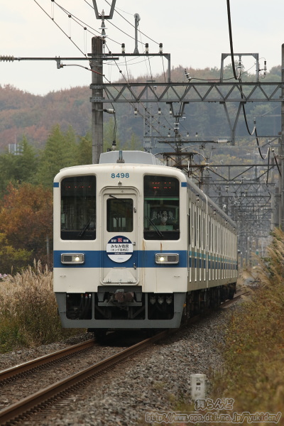 晩秋の丘陵地を行く新駅開業記念のヘッドマークを付けた8198F